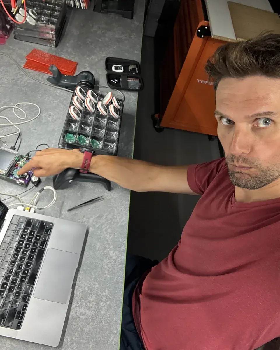 Mariusz Smenżyk at his workbench with a laptop, a prototype board and a tray of Vimo Swim devices